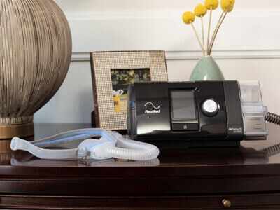A ResMed CPAP device and mask on a bedside table.