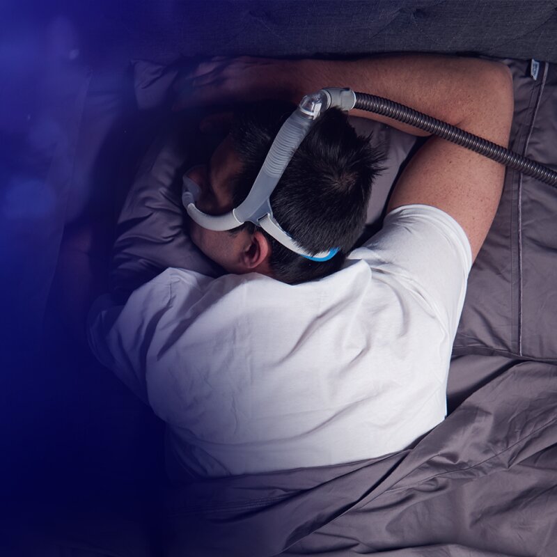 Man laying on his stomach and wearing Resmed's AirFit N30i CPAP Mask while sleeping beside his partner