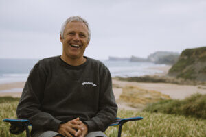 Professional surfer Dani Garcia laughing while sitting on a camp chair by a beach as he talks about his life before and after CPAP therapy.