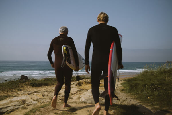 Surfer Dani and his son walking along the beach towards the waves carrying their surfboards.