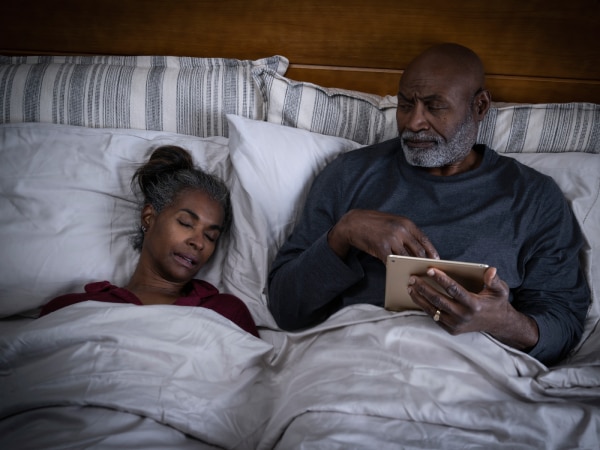  woman snoring in bed as partner looks annoyed